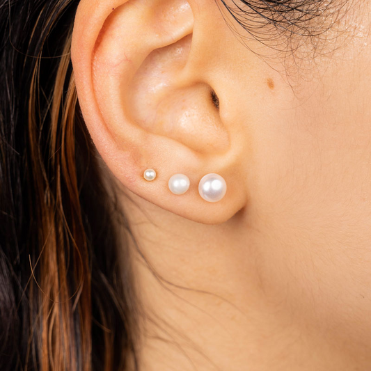 Drei Ohrringe mit Süßwasserperlen in verschiedenen Größen, Edelstahlstecker, getragen am Ohrläppchen.