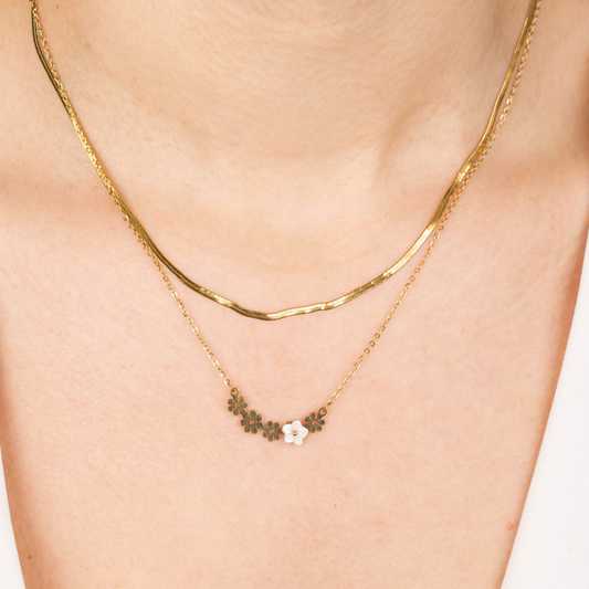 Zwei goldene Edelstahl-Halsketten, eine glatt, die andere mit Blumenmotiv, auf Hals getragen