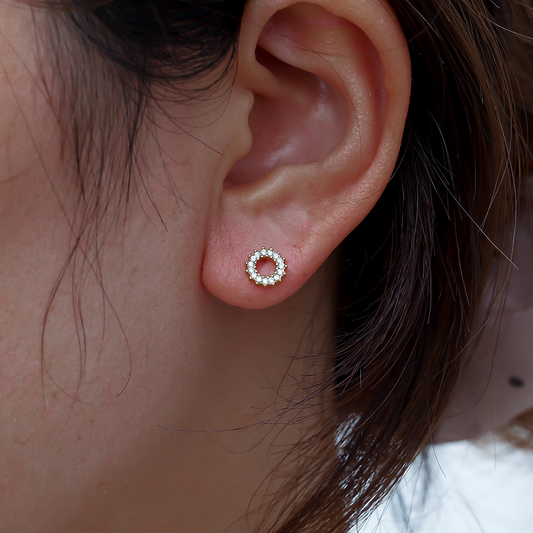Kreisförmiger Edelstahl-Ohrring mit Blumenmotiv und Diamantakzenten am Ohr getragen