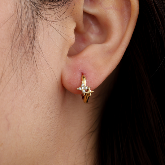 Goldene Edelstahl-Creolen mit vierzackigem Sternmotiv und kleinen Diamanten, getragen am Ohr.