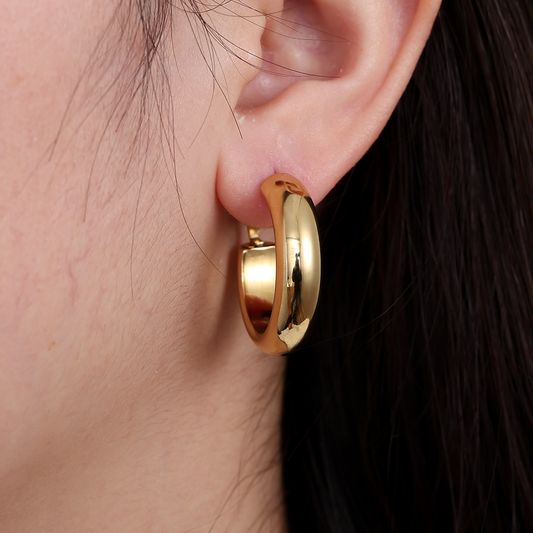 Goldfarbene Edelstahl-Creolen am Ohr, glänzende Oberfläche, runde Form, schlichtes Design