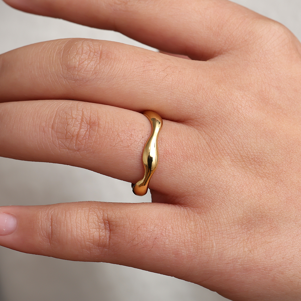 Goldener Edelstahlring mit wellenförmigem Design, getragen an einem Finger. Glänzende Oberfläche, schlichte Eleganz.
