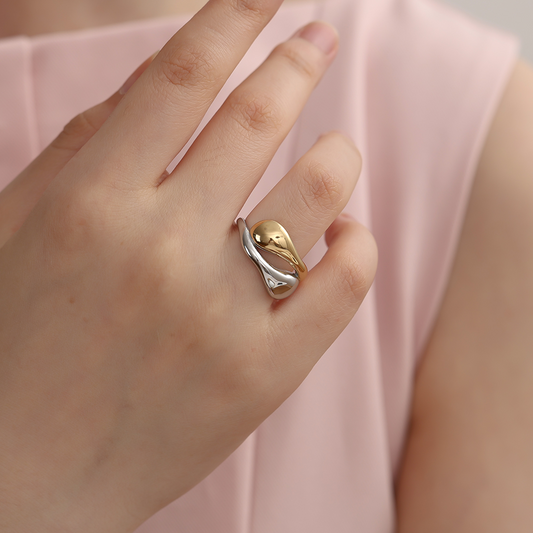 Cycle Drops Edelstahlring in Silber und Gold, organische Form, getragen an der Hand einer Person in rosa Oberteil