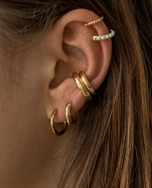 Goldfarbene Edelstahl-Ohrringe in Creolenform am Ohr, kombiniert mit einem Perlen- und einem gedrehten Ohrklemme-Design.