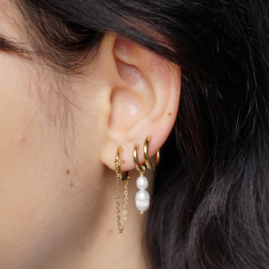 Goldene Edelstahl-Ohrringe mit hängender Kette und Perlenanhänger am Ohr getragen.