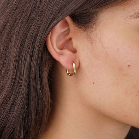 Goldfarbene, quadratische Edelstahl-Ohrringe mit abgerundeten Kanten am Ohr einer Person