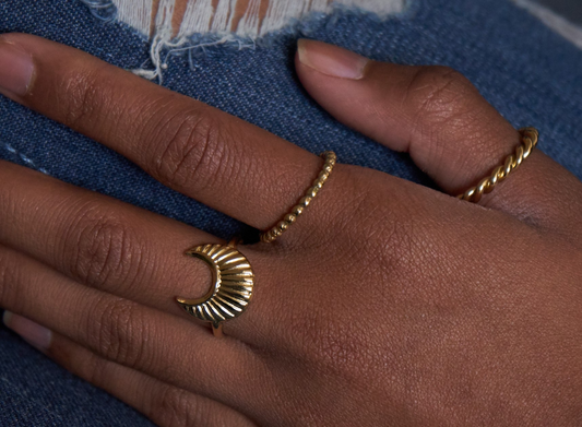 Goldfarbener Edelstahlring mit kleinen Punkten, getragen an der Hand, neben zwei weiteren Ringen auf Jeansstoff.