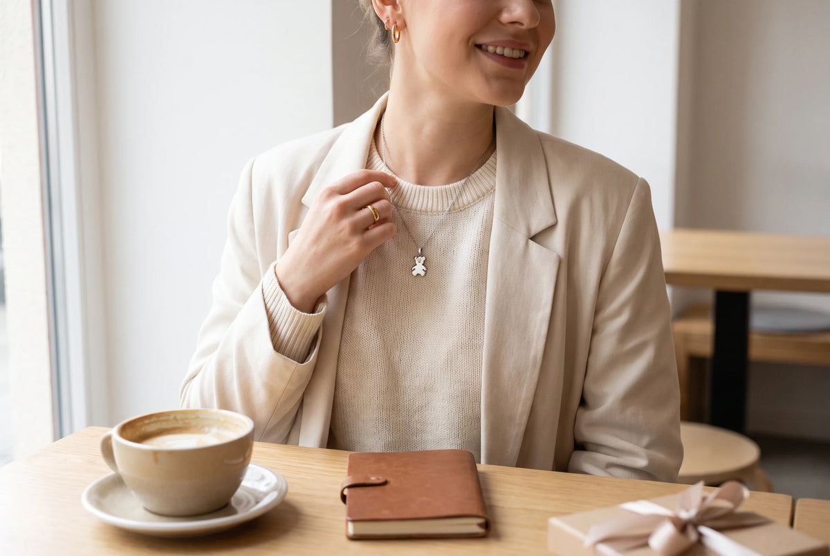 Junge Frau auf dem morgendlichen Weg zu ihrem ersten Tag trägt eine feine Edelstahlkette mit kleinem Bärenanhänger zu Hemd, Strickweste und Laptoptasche.