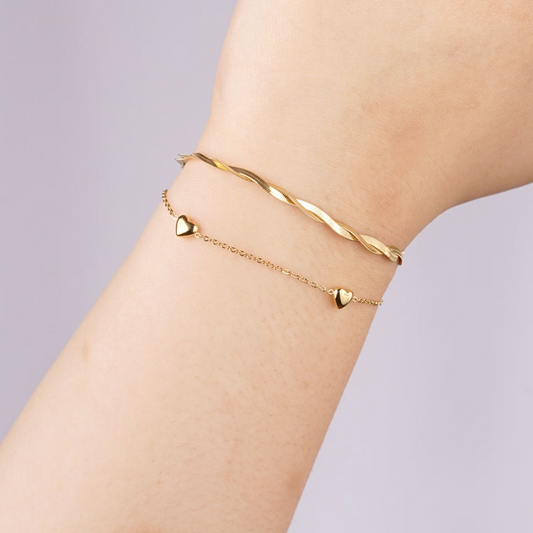 Goldfarbenes Edelstahlarmband mit drei kleinen Herzanhängern, filigrane Kette, getragen am Handgelenk.
