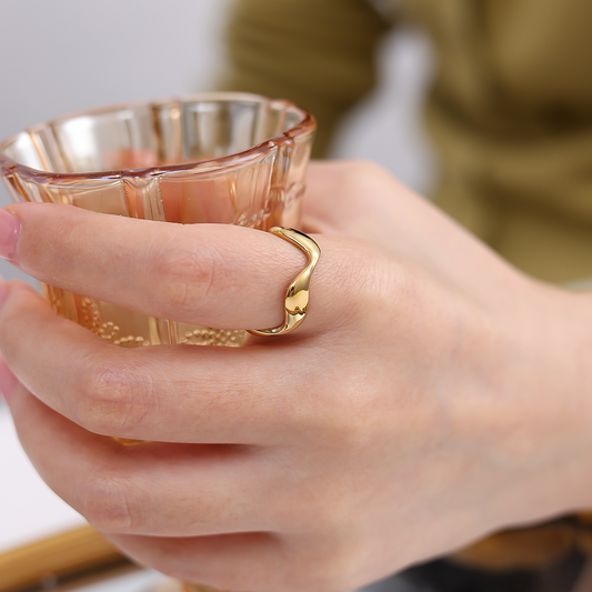 Goldfarbener Edelstahlring in Wellenform an Finger, hält ein Glas