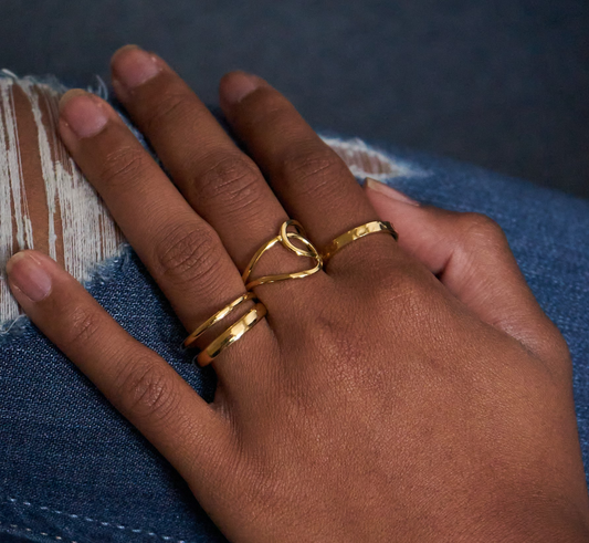 Zweischichtiger Edelstahlring in Goldoptik, getragen an der Hand, kombiniert mit anderen goldenen Ringen, auf Jeanshintergrund