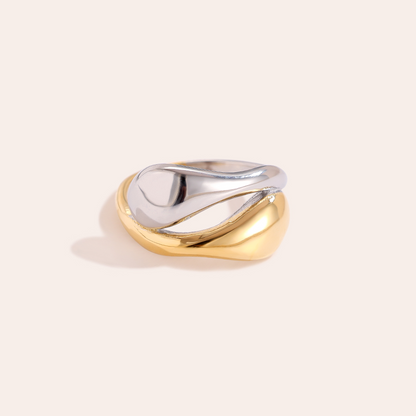 Zwei ineinander verschlungene Edelstahlringe, einer in Gold, der andere in Silber, mit geschwungenem Design.